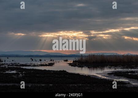 Rayons de soleil au coucher du soleil, avec des nuages sombres en arrière-plan, au-dessus du lac Trasimeno, Ombrie, Italie Banque D'Images