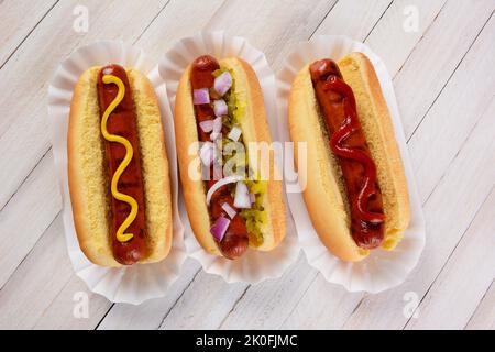 Vue de dessus de trois hot dogs sur une table en bois avec différents condiments. Banque D'Images