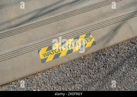 Collé regarder votre panneau autocollant de pas sur un pas de béton à Tucson, Arizona. Vue d'un panneau noir et jaune sur un escalier à deux marches depuis le dessus. Banque D'Images