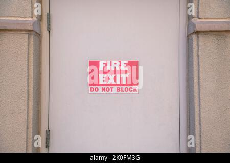 Sortie d'incendie ne pas bloquer sur une porte beige au centre-ville de Tucson, Arizona. Gros plan d'un panneau de sortie de secours sur une porte avec des charnières latérales entre le béton wa Banque D'Images