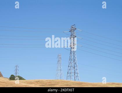 Tours électriques métalliques avec lignes électriques qui les traversent sur une colline, herbe brune. Risque d'incendie élevé Banque D'Images