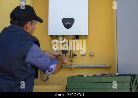 Plomber sur une échelle pendant la réparation et l'entretien d'une chaudière à gaz en prévision de l'hiver. Remplacement d'une tuyauterie de chauffage central Banque D'Images