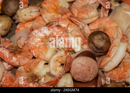 De délicieuses crevettes cuites entourées de saucisses, de champignons et d'oignons dans l'ébullition des fruits de mer - attention sélective Banque D'Images