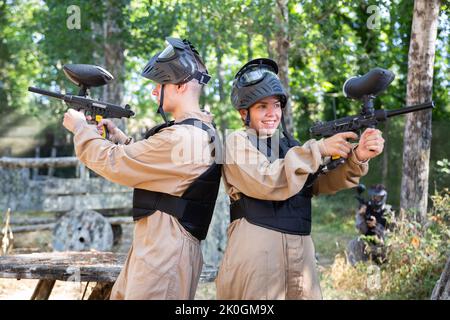 Des joueurs de paintball de garçon et de fille se tenant dos à dos et tirant Banque D'Images