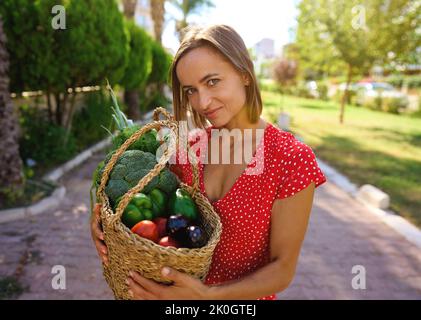 Femme tenant une boîte en bois pleine de légumes frais crus. Panier de fruits et légumes avec poivrons, tomates, brocoli, pêches à la banane, raisin dans le Banque D'Images