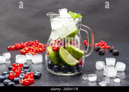 Verseuse en verre avec baies, glace et citron vert. Des branches de cassis, de glace et de myrtille sont sur la table. Copier l'espace. Arrière-plan noir. Banque D'Images