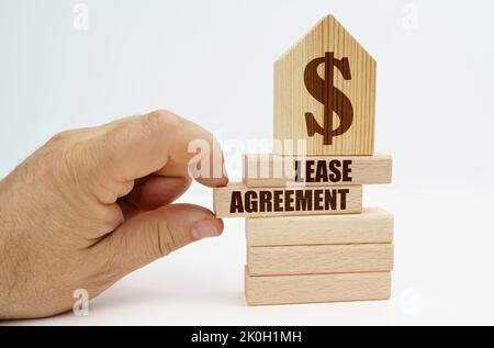 Immobilier et affaires. Sur les blocs de bois avec l'inscription - Contrat de location, il y a un modèle de maison avec un symbole de dollar. La main de l'homme ta Banque D'Images
