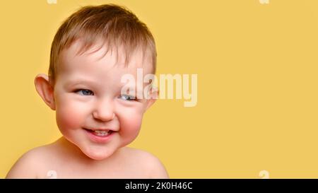 Sly enfant, fond jaune studio, espace de copie. Portrait d'un enfant insidieux aux joues rouges. Enfant âgé de un an et deux mois Banque D'Images