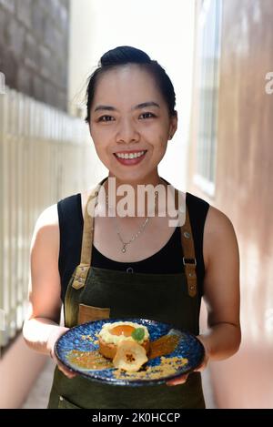 Femme vietnamienne serveuse en tablier tenant une tarte aux pommes sur une assiette bleue Banque D'Images