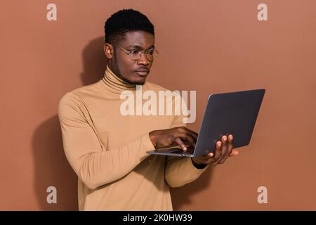 Portrait de l'attrayant, spécialisé, intelligent et intelligent gars à l'aide d'un ordinateur portable développement de projet Web démarrage isolé sur fond de couleur marron Banque D'Images