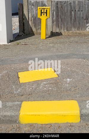 Important travail d'entretien et de peinture par la brigade des pompiers d'Essex de l'approvisionnement en eau souterraine incendie et borne d'eau jaune pour trou d'homme et marqueur de bordure Angleterre Royaume-Uni Banque D'Images