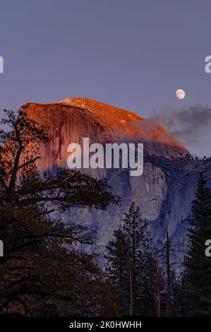 Photo verticale d'un beau coucher de soleil sur le sommet de la montagne Half Dome avec la lune dans le ciel Banque D'Images