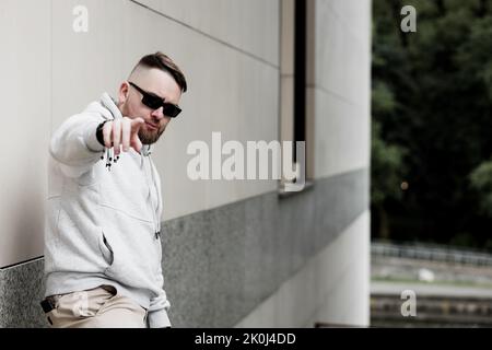 Un homme cool dans un sweat à capuche debout dans la rue et pointant son doigt vers vous Banque D'Images