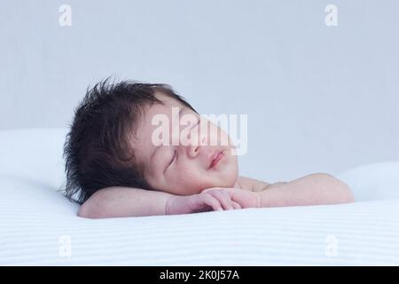 Bébé dormant sur un coussin , reposant sa tête sur ses bras dans une position mignonne Banque D'Images