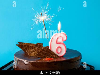 Numéro 6 bougie d'anniversaire brûlant et flambeur avec des étincelles mouche sur le gâteau. Concept de célébration du sixième anniversaire. Beaucoup d'espace de copie sur bleu. Banque D'Images