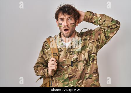 Jeune homme hispanique portant un uniforme militaire de camouflage fou et effrayé avec les mains sur la tête, peur et surpris de choc avec la bouche ouverte Banque D'Images