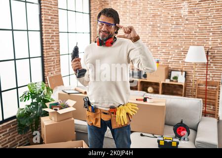 Beau homme d'âge moyen tenant un tournevis à la nouvelle maison souriant et confiant gestante avec la main faisant un petit signe de taille avec les doigts regardant et le c Banque D'Images