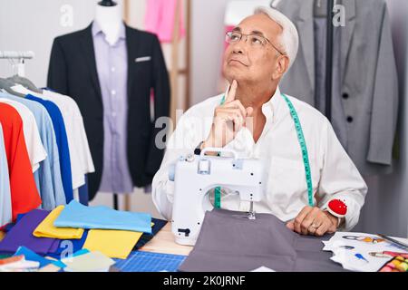 Homme d'âge moyen avec coiffeur de cheveux gris utilisant la machine à coudre pensant concentré sur le doute avec le doigt sur le menton et regardant vers le haut se demandant Banque D'Images