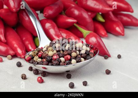 Piment et cuillère en métal avec poivrons rouges, noirs et blancs. Banque D'Images