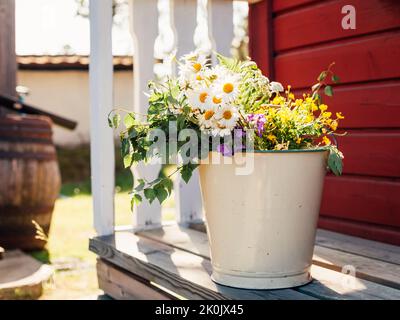 Bouquet de fleurs sauvages du milieu de l'été dans un seau en émail sur patio en Suède, lumière naturelle d'été scandinave Banque D'Images
