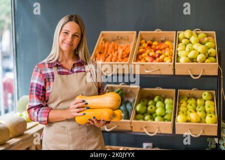 Femme travaille dans la boutique de fruits et légumes. Elle tient le panier avec de la courge de noyer cendré. Banque D'Images