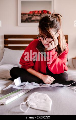 Corps entier de la notice d'instruction de lecture de la femelle concentrée de test rapide d'antigène tout en étant assis sur le lit avec un masque médical pendant la pandémie de COVID Banque D'Images