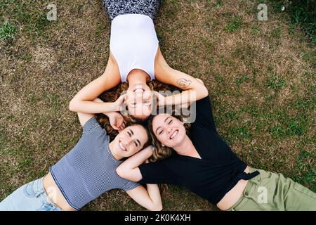 D'en haut souriantes femmes amicales plaçant dans le cercle avec la tête couché sur l'herbe et appréciant le temps sur la prairie Banque D'Images