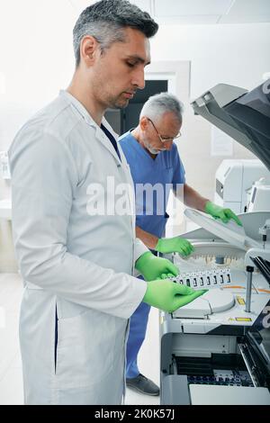 Techniciens de laboratoire travaillant en laboratoire médical et effectuant des recherches sur des échantillons de sang à l'aide de technologies modernes et de machines de recherche médicale Banque D'Images