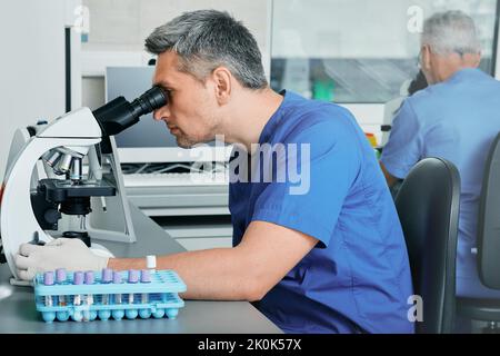 Deux scientifiques masculins qui cherchent des microscopes tout en travaillant à la recherche médicale sur le sang dans un laboratoire médical scientifique Banque D'Images