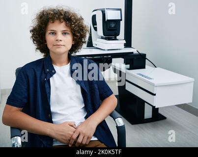 Mignon garçon assis dans la clinique d'ophtalmologie près de l'équipement ophtalmique pour l'examen des yeux. L'ophtalmologiste vérifie l'acuité visuelle de l'enfant en utilisant l'autore Banque D'Images