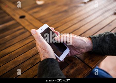 Homme âgé utilisant son smartphone assis à la table de sa maison Banque D'Images