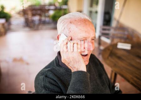 Homme âgé parlant au téléphone sur le porche de sa maison Banque D'Images