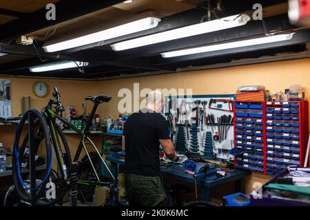 Vue arrière de chauve homme debout près de l'atelier tout en fixant le vélo dans le garage professionnel moderne Banque D'Images