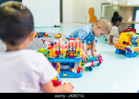 Développement de l'imagination et de la créativité. Croissance cognitive. Tout-petits garçons jouant avec des jouets en plastique et une voiture colorée dans une salle de jeux de la garderie. Banque D'Images