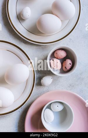 D'en haut encore la vie de beaux oeufs de Pâques peints sur les bols et les assiettes sur fond blanc de table Banque D'Images