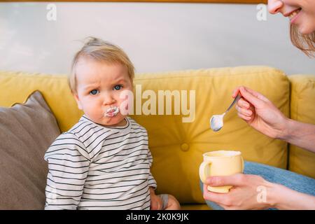 Maman nourrit un petit enfant à la maison avec du yaourt à la cuillère. Concept de famille Banque D'Images