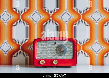 Radio rouge vintage sur table contre mur avec des formes géométriques blanches et orange Banque D'Images