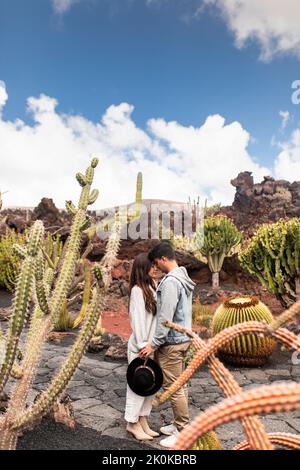 Vue latérale d'un jeune homme et d'une jeune femme d'origine ethnique dans des tenues élégantes qui touchent les têtes tout en restant debout sur la route dans le jardin exotique de Cactus dans le village de Guatiza Banque D'Images