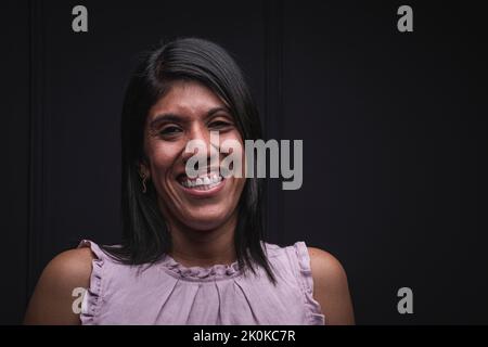 Positive self assured jeune Latino femme portant un chemisier décontracté souriant et regardant l'appareil photo tout en se tenant sur fond noir Banque D'Images