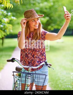 Ne laissez rien derrière vous dans la nature, mais des souvenirs. Une jeune femme qui prend un selfie tout en étant dehors pour une balade en vélo dans le parc. Banque D'Images