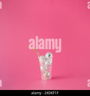 Gobelet en plastique transparent rempli de boules disco brillantes et de paille dorée sur fond rose. Banque D'Images