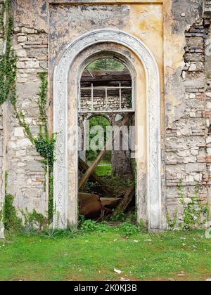 Vue à travers la porte voûtée d'une fenêtre cassée dans un vieux bâtiment abandonné surcultivé Banque D'Images