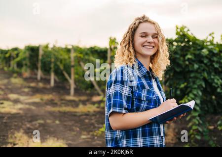 Gros plan portrait d'un agronome caucasien souriant recherchant la plantation de vignes et l'écriture résultats dans le carnet. Une agriculture intelligente. Technologie agricole Banque D'Images