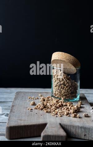 Bocal en verre avec granola de noyer posé sur une planche à découper en bois sur fond noir Banque D'Images