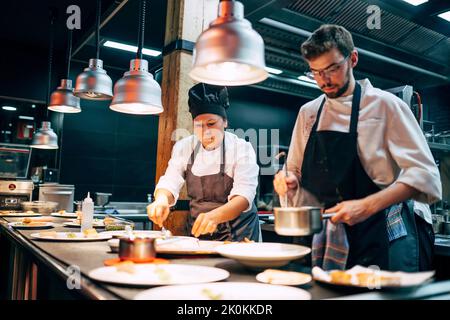 Homme et femme en tabliers travaillant dans le restaurant sur la cuisine et préparant la nourriture pour les clients Banque D'Images