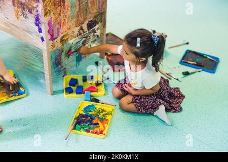 Peinture de film adhésif. Petite fille enfant peinture avec une éponge et peint sur un film adhésif enroulé tout autour de l'étagère en bois. Activité créative pour le développement des enfants à l'école maternelle. Photo de haute qualité Banque D'Images