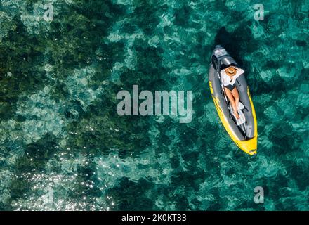 Une femme solitaire dans un chapeau de paille se détendant dans le kayak gonflable flottant sur les vagues turquoise de la mer Adriatique. Vue aérienne du dessus de la côte. Exotique c Banque D'Images