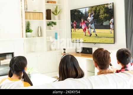 Divers groupes d'enfants assis sur le canapé et regardant un match de football Banque D'Images