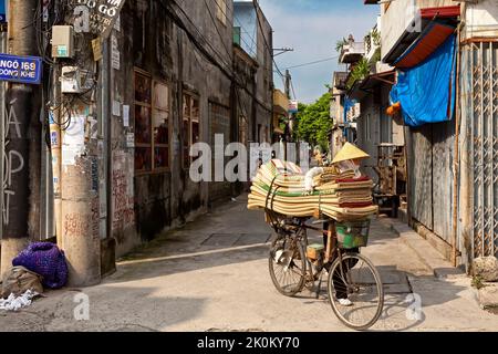 Un motard vietnamien portant un chapeau de bambou vendant des tapis d'un vélo, Hai Phong, Vietnam Banque D'Images