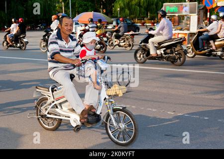 Homme portant bébé sur vélo électrique dans la circulation, Hai Phong, Vietnam Banque D'Images